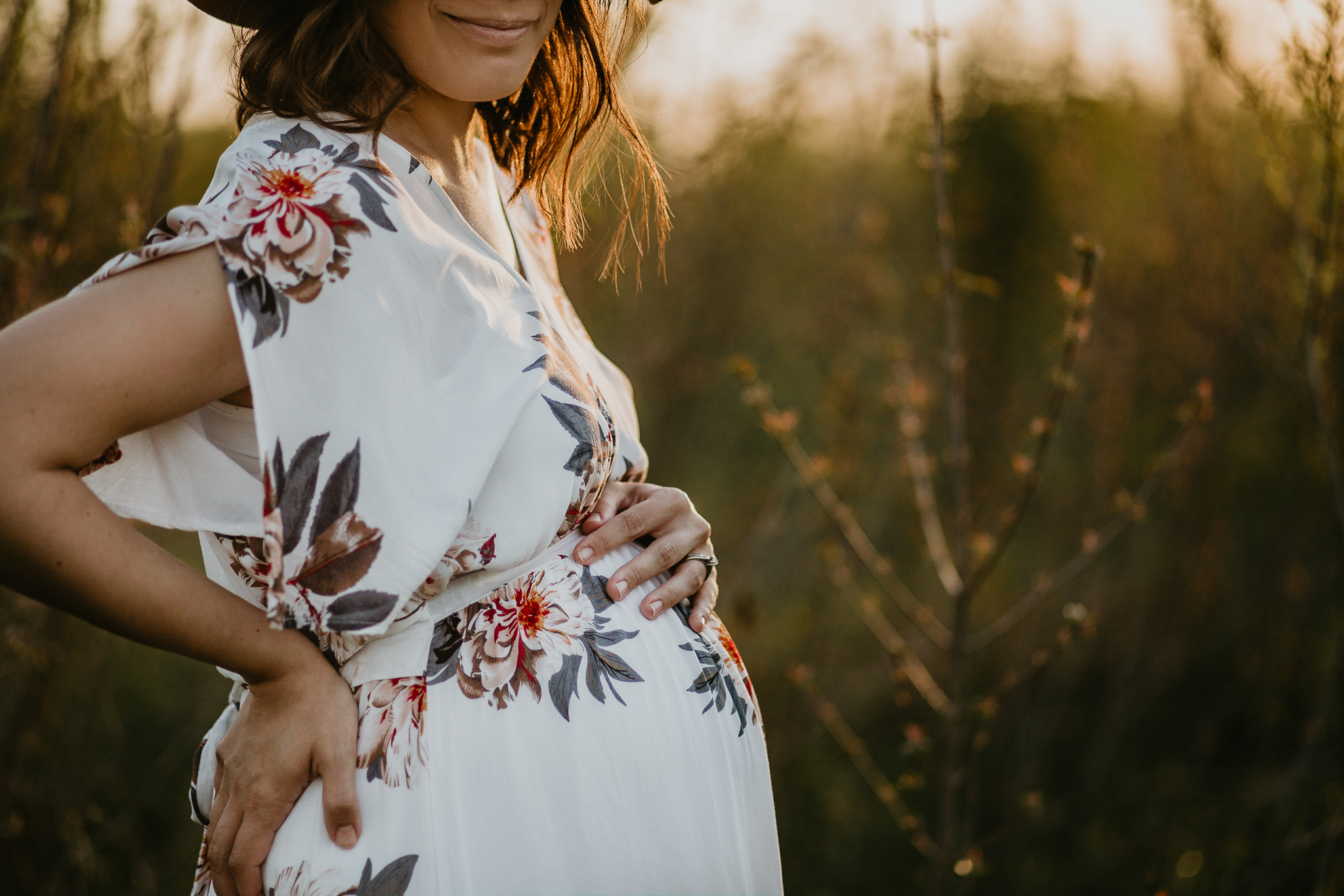 Expecting woman in a sun hat holding her belly in a golden field of grasses.